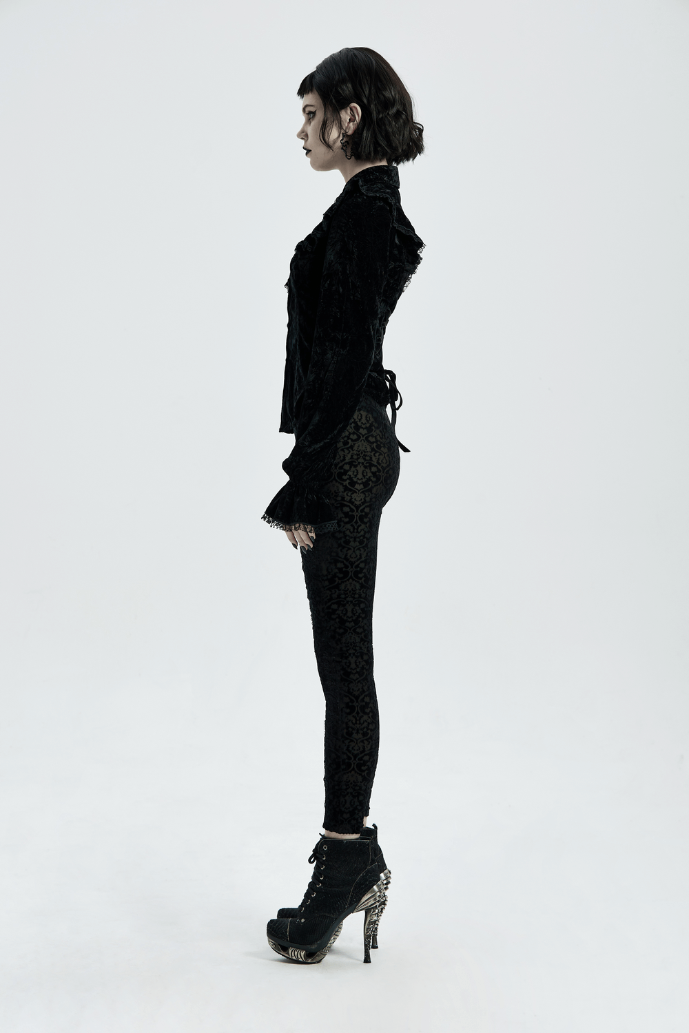 Elegant woman in black gothic velvet leggings with floral lace detail, showcasing a stylish side view.
